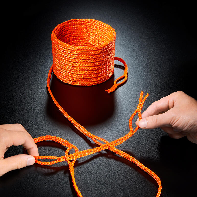 Orangefarbenes Schlaufenseil auf schwarzem Untergrund, eine Hand bindet einen Knoten.