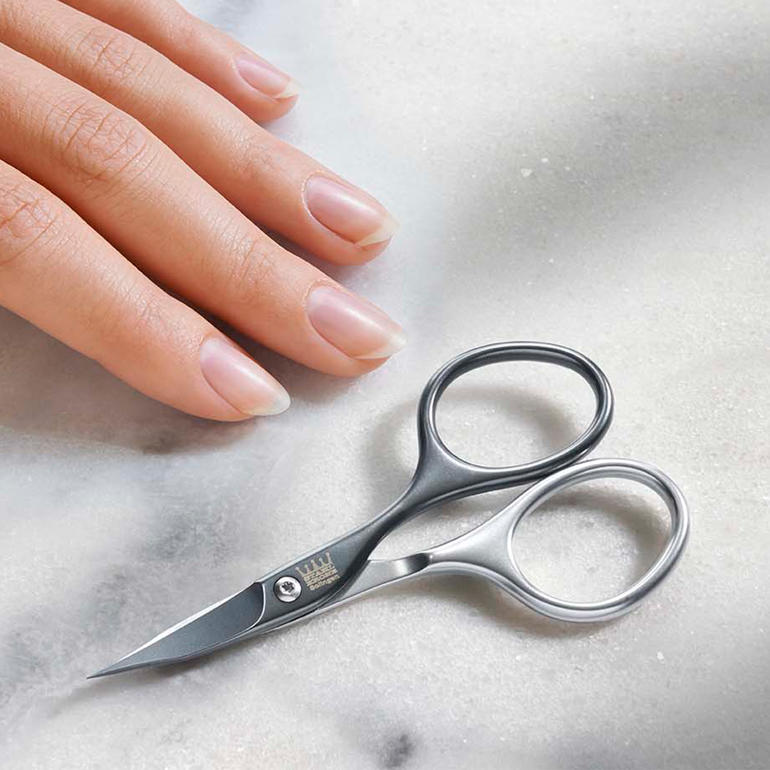 Selbstschärfende Maniküre-Schere auf einem Tisch neben einer Hand.