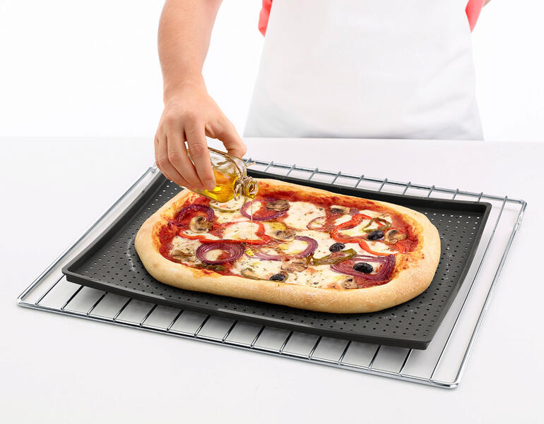 Person ölt eine Pizza auf einer knusprigen Backmatte