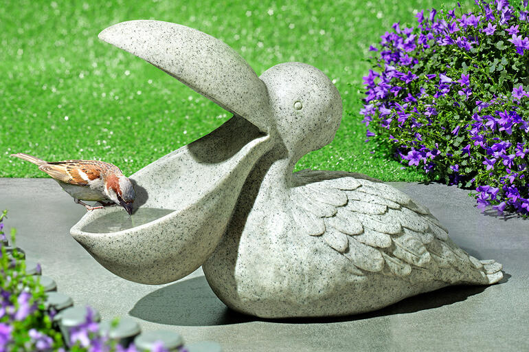 Vogeltränke in Form eines Pelikans aus Stein auf grünem Rasen.