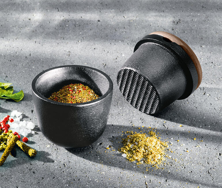 Gusseisen-Mörser mit Gewürzen auf dem Tisch.