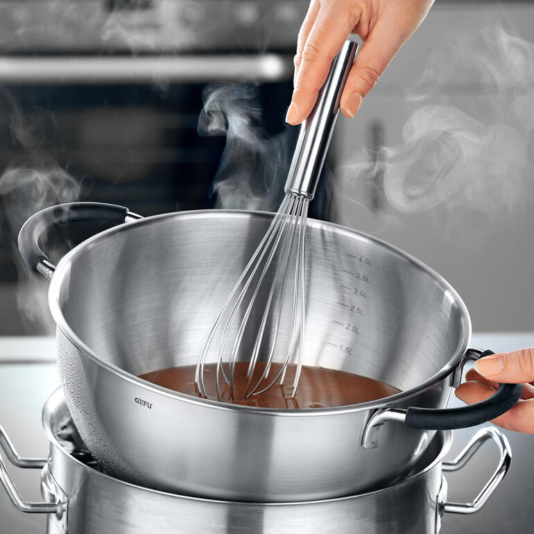 Placé sur un bain-marie, le bol est très pratique pour faire fondre du chocolat. Hand mit einem Schneebesen in einer dampfenden Rührschüssel über dem Wasserbad.