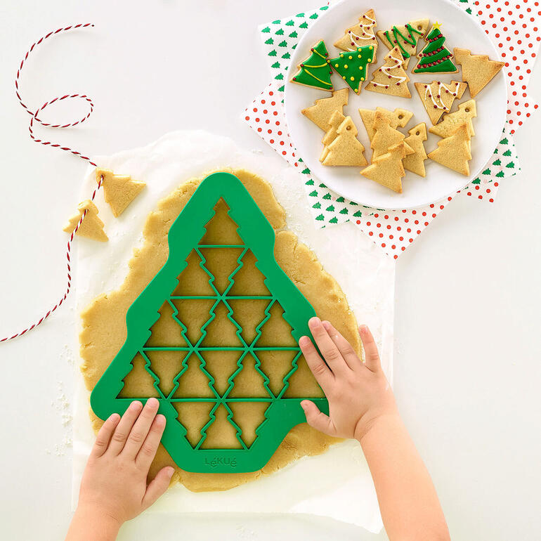 Hände rollen Teig für Weihnachtsbaum-Plätzchen aus.