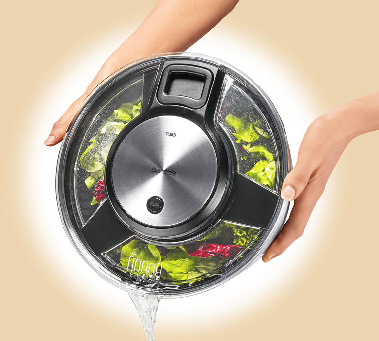 Nutzer hält die Salatschleuder mit dem Deckel oben und frischem Gemüse innen.