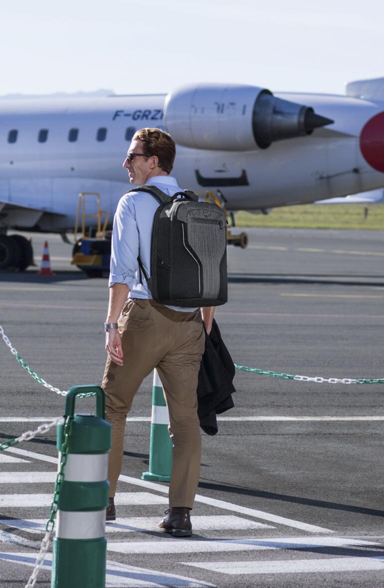 Mann mit Rucksack am Flughafen vor einem Flugzeug.