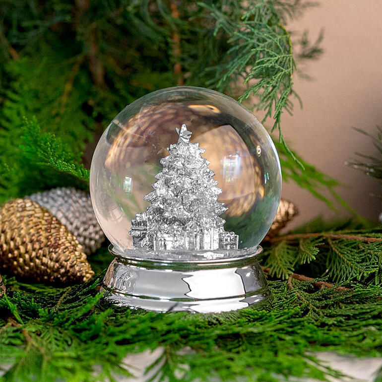 Versilberte Schneekugel mit einem Weihnachtsbaum im Inneren auf grüner Dekoration