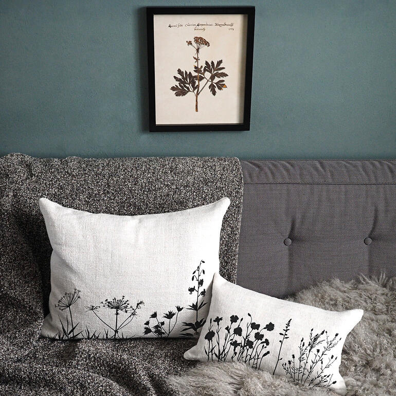 Coussin en lin de 100 ans Zwei Leinenkissen mit schwarzen Pflanzenmustern auf einer Couch, ein Bild hängt darüber.