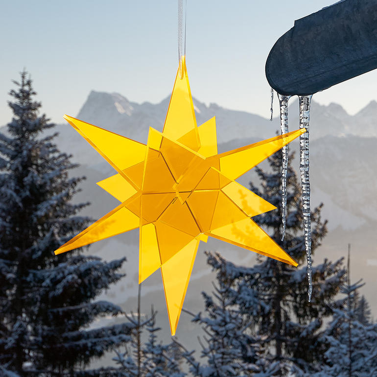 Gelber Sternen-Sonnenfänger hängt an einem Vordach mit verschneitem Hintergrund