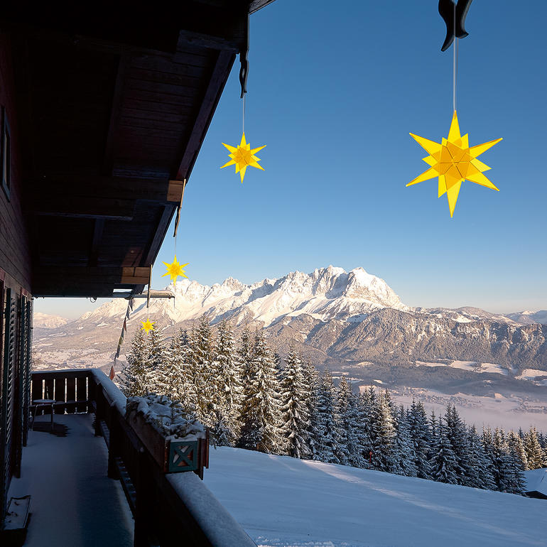 Gelbe Sterne hängen an einem Balkon mit Berglandschaft im Hintergrund
