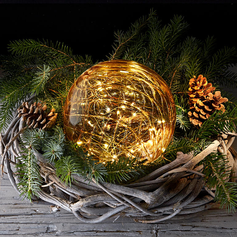 Tinted glass ball mit Mikro-LEDs, umgeben von Tannenzweigen