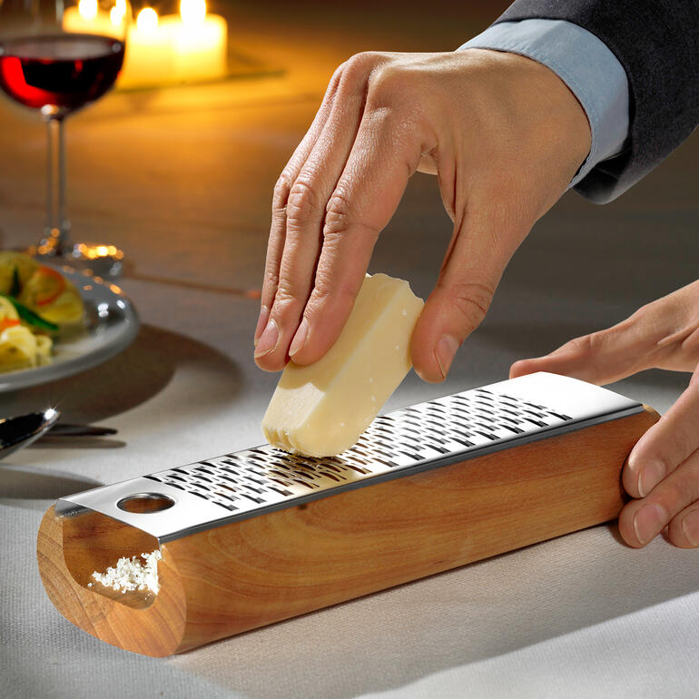 Mann reibt Käse auf einem Design-Käsereiber aus Holz.