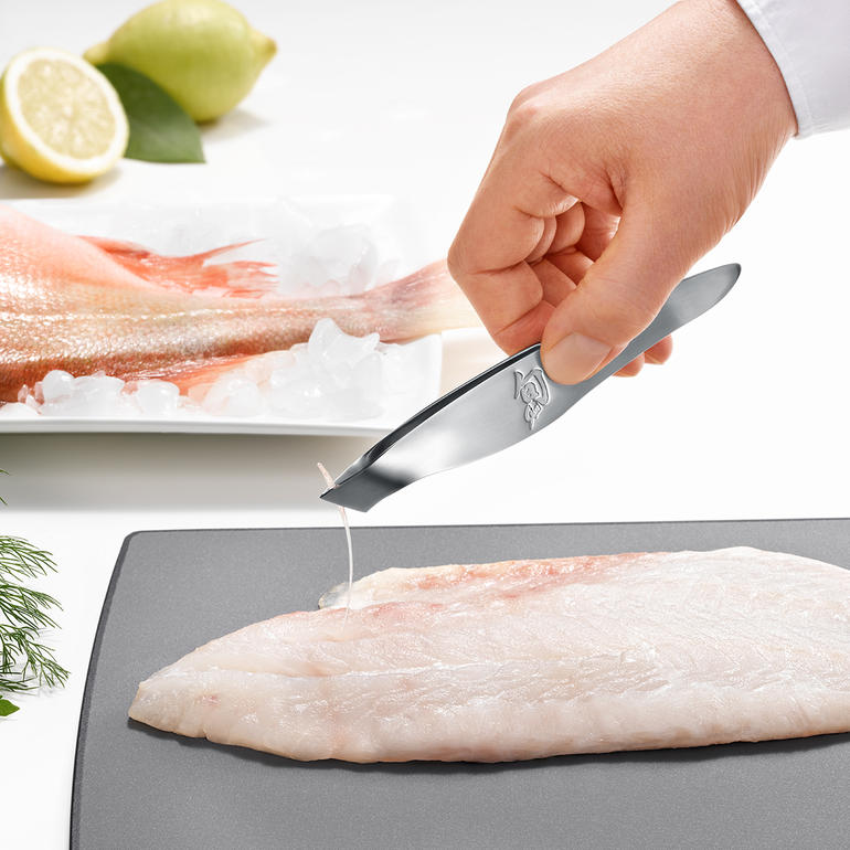 Hand entfernt eine Fischgräte mit einer KAI Grätenpinzette.