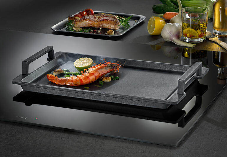 Teppanyaki-Platte mit Garnelen und Gemüse auf einem Kochfeld.