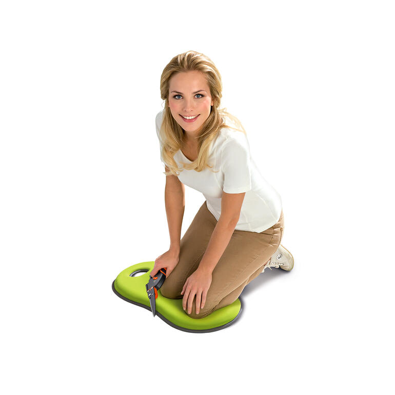 Frau kniet auf einem grünen Knie- und Sitzkissen im Garten.