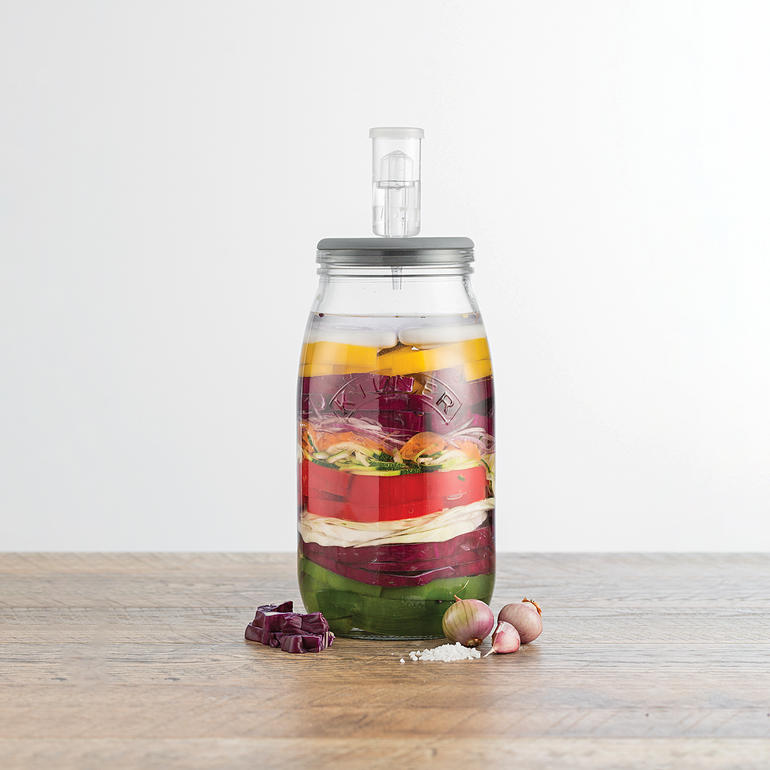 Fermentierglas mit Gärventil, gefüllt mit buntem Gemüse in Schichten.