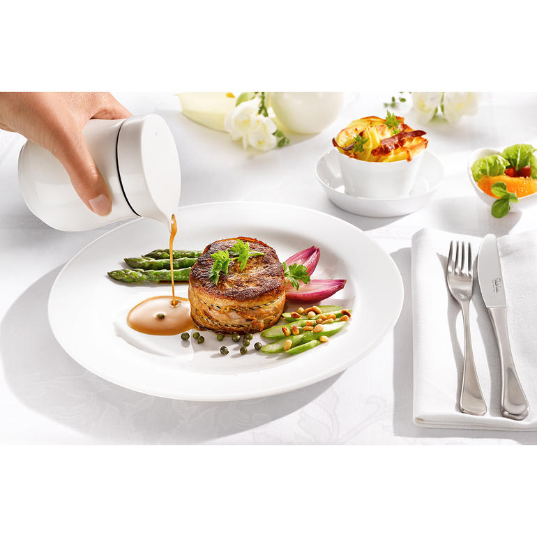 Frau serviert Sauce mit einer Thermo-Sauciere auf einem Teller.