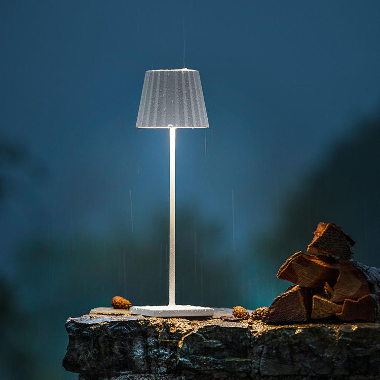 Design Akku-Tischleuchte mit stilvollem Schirm auf einem Stein.