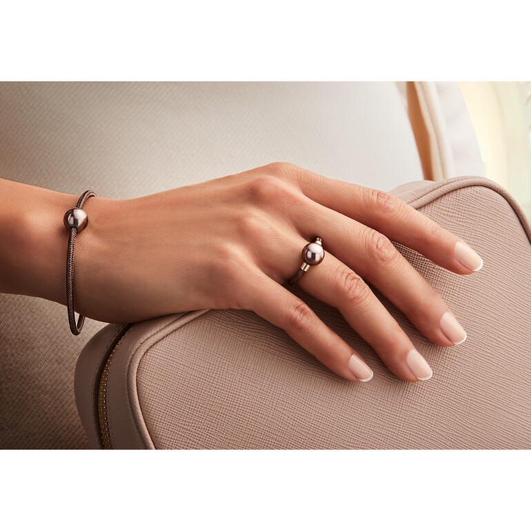 Hand, die eine roségoldene Armbänder und Ring mit schwarzer Perle auf einer Tasche hält.