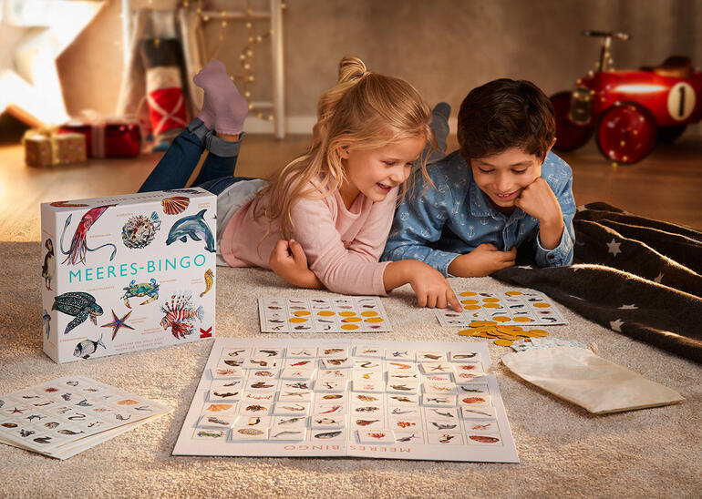 Kinder spielen Meeres-Bingo auf dem Boden mit Spielmaterial.