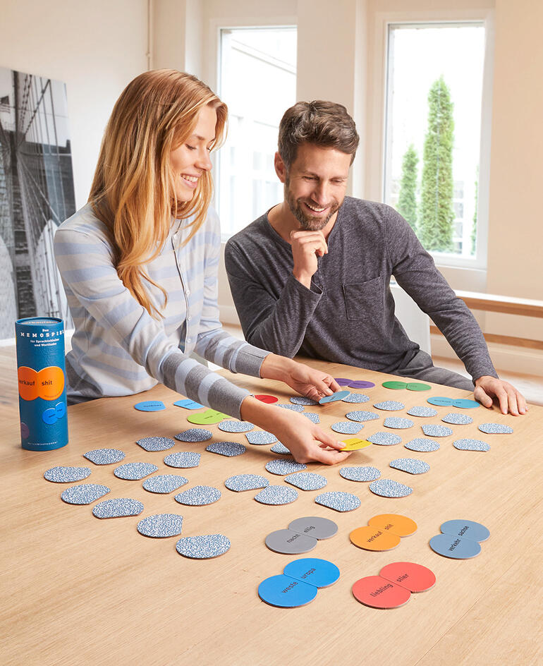 Paar spielt ein Memo-Spiel mit bunten Karten auf einem Tisch.