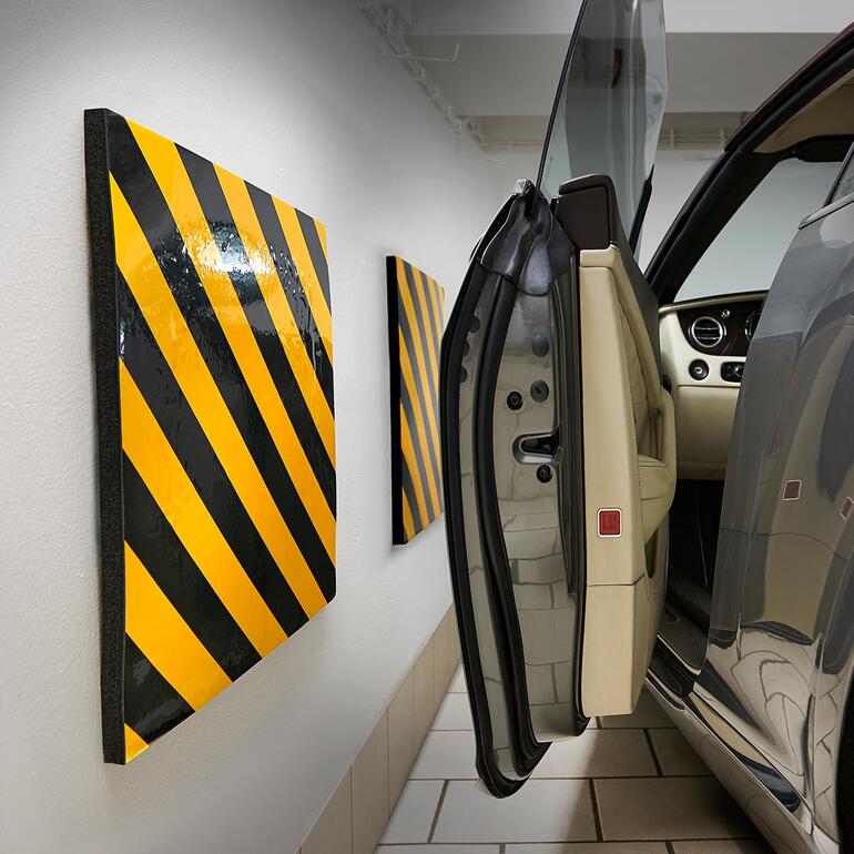 Garagenwand-Polster mit gelb-schwarzen Streifen neben einem geöffneten Autotür.