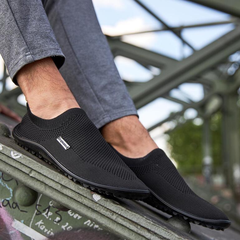 Schwarzer Barfuß-leguano® Slipper an einem Fuß, auf einem Metallgerüst.