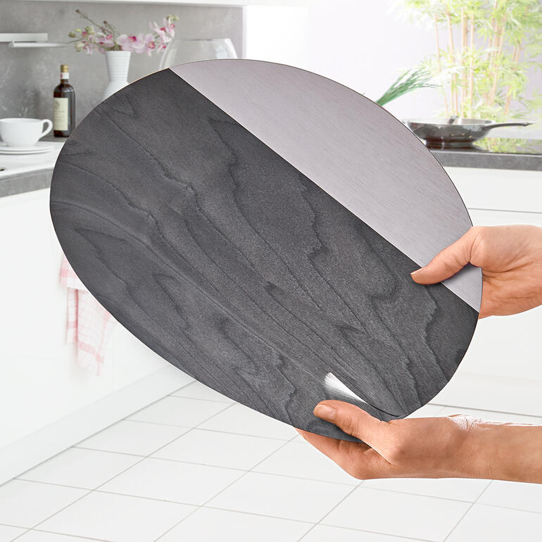 Hand hält das ovalen Tischset aus Holz mit silberner und schwarzer Oberfläche.