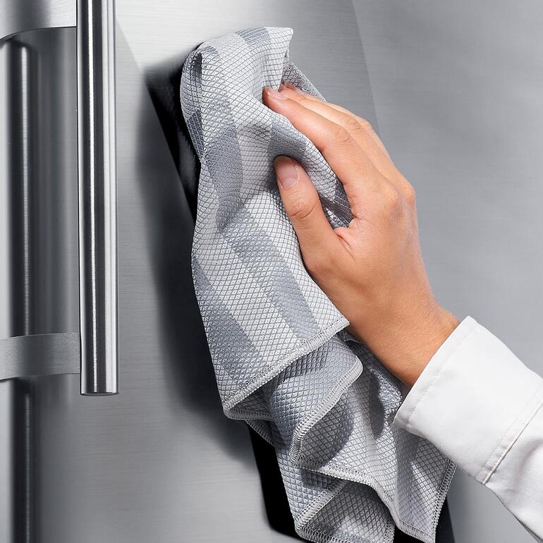 Händchen reinigt einen Edelstahlkühlschrank mit einem grauen Universaltuch.