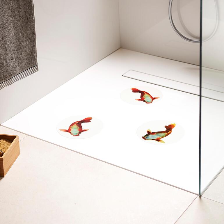 Drei rutschfeste Tattoos in Form von Koi-Fischen auf einem Badezimmerboden.