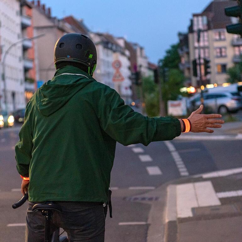 Radfahrer mit Leuchtarmband, der ein Handzeichen gibt.