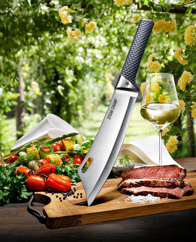 SteakChamp Kochmesser von oben, umgeben von Gemüse und Fleisch auf einem Holzbrett.
