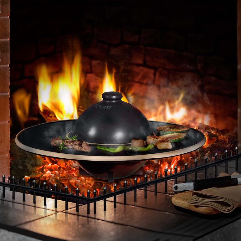 RÖMERTOPF BBQ Planet mit köchelndem Essen über einem offenen Feuer.