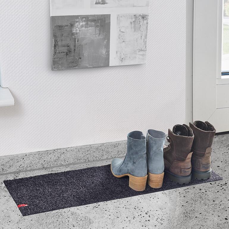 Schwarze Fußmatte neben Stiefeln im Flur.
