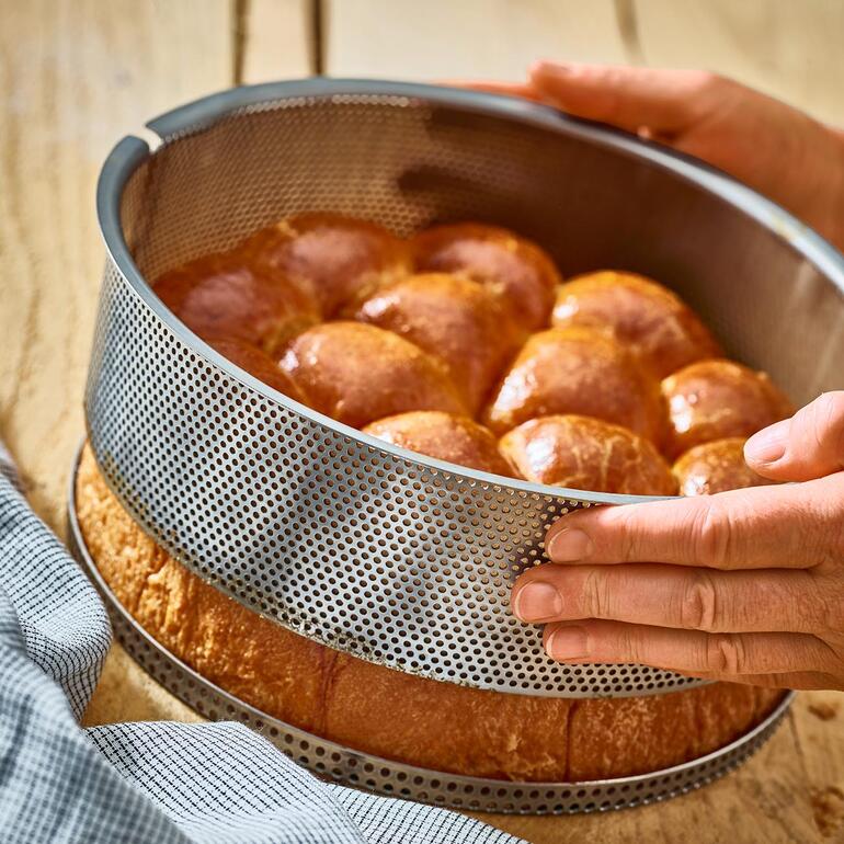 Den Ring der Kuchenform können Sie ganz bequem vom separaten Lochboden abheben. Perforierte Edelstahl-Backform mit frisch gebackenem Brot.