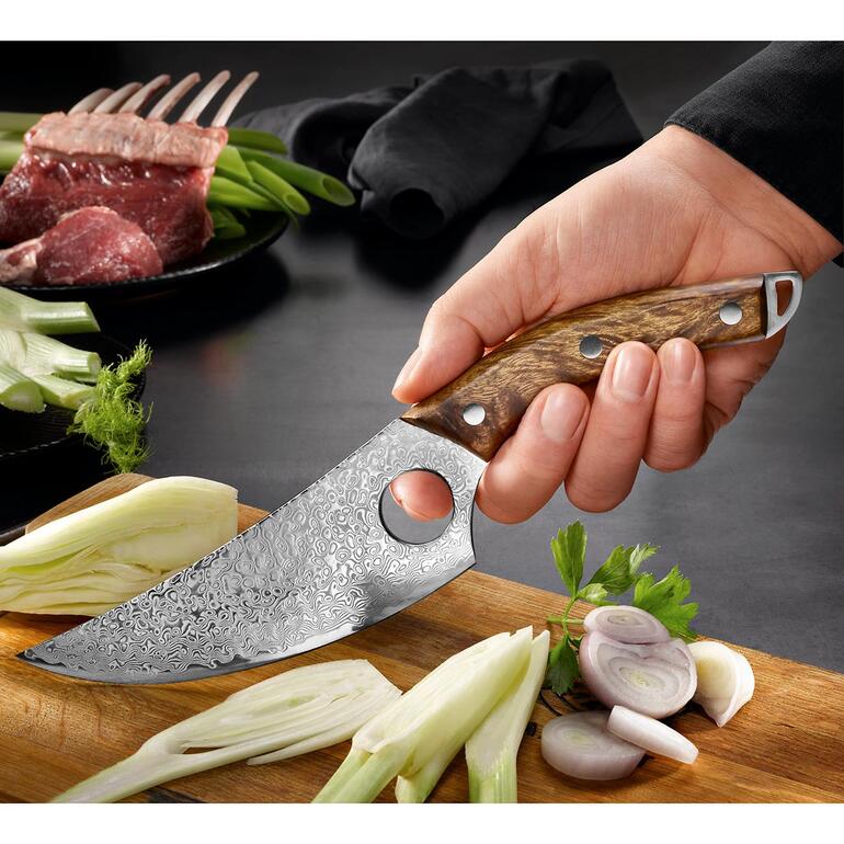 Damast Butcher-Messer in der Hand mit frischen Zutaten im Hintergrund.