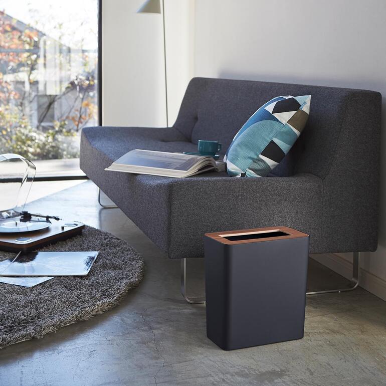Schwarzer Abfallbehälter neben einer Couch in einem modernen Raum.