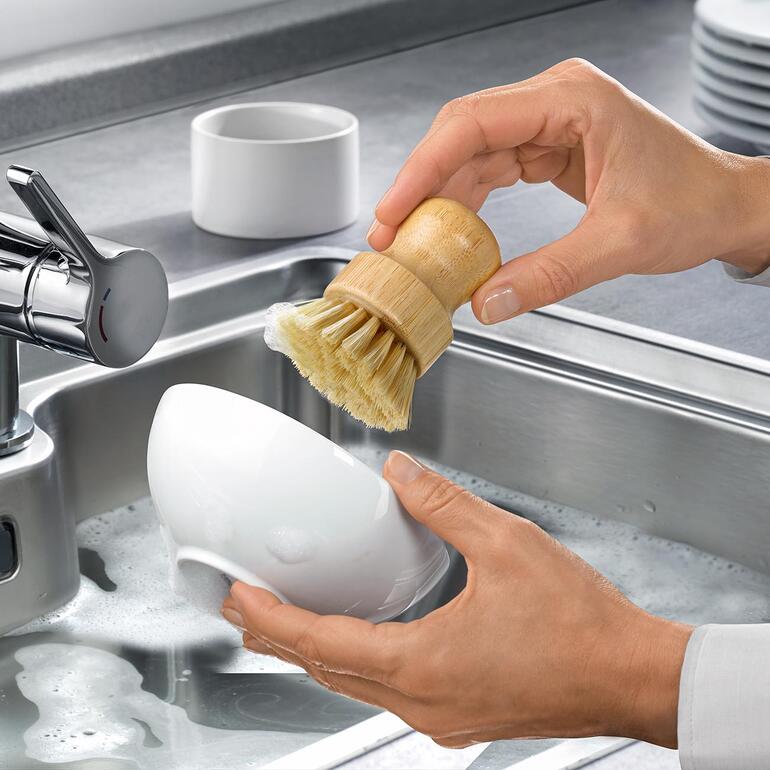 Hände verwenden eine nachhaltige Spülbürste in der Spüle.