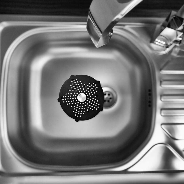 Das handtellergrosse Abflusssieb ist perfekt in der Spüle, Dusche, Wanne, über dem Bodenabfluss, ... Schwarzes Abflusssieb schwebt über einer Spüle