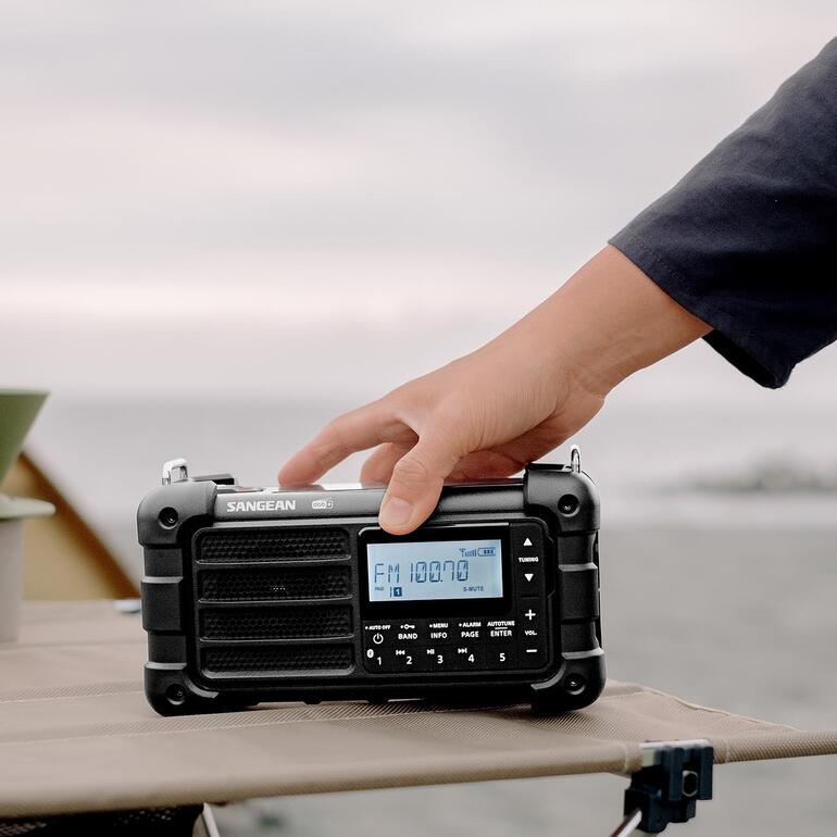 Hand hält digitales Survival-Radio mit LCD-Display bei outdoor-Aktivität.
