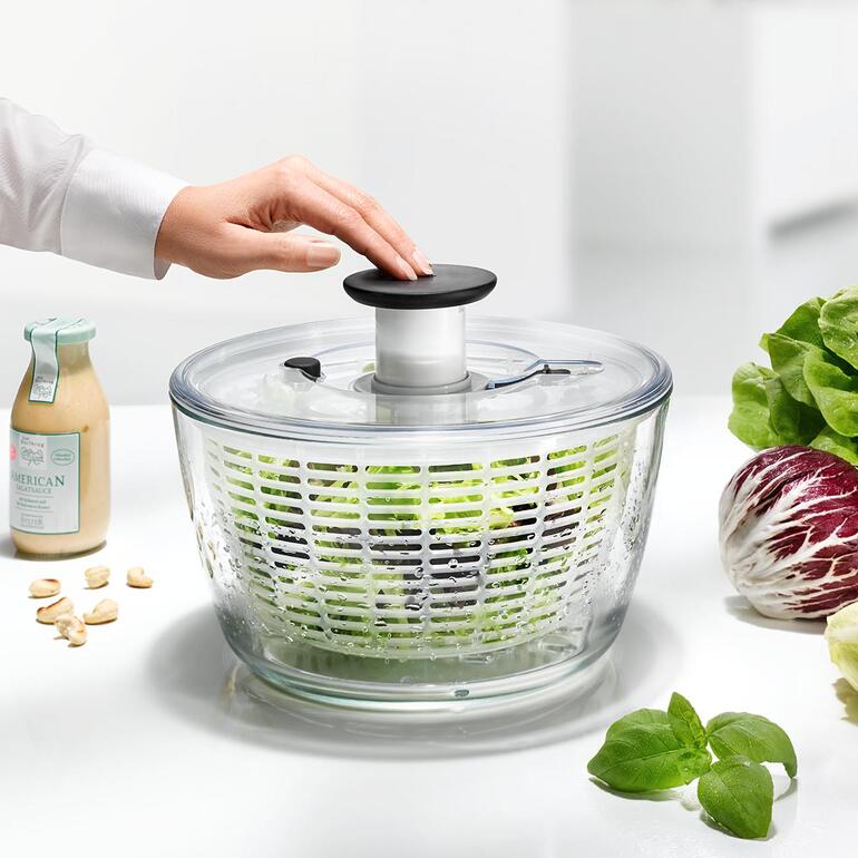 Frau dreht den Deckel einer Salatschleuder aus Glas mit frischem Salat.