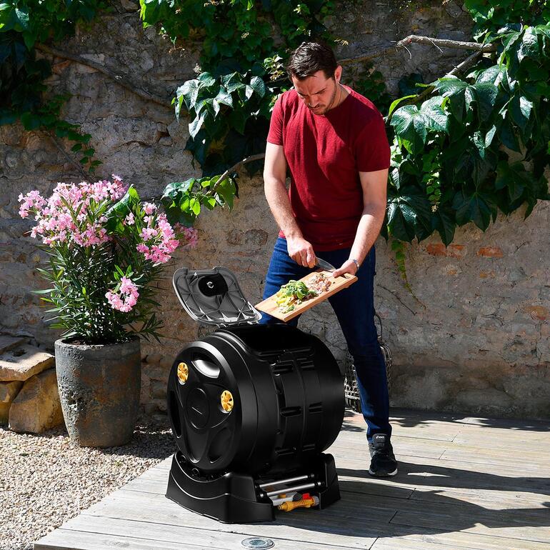 Mann bringt Küchenabfälle in einen 2-in-1 Trommelkomposter im Garten.