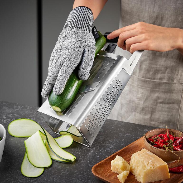 Hand an einer Turmreibe, die eine Zucchini zum Raspeln verwendet.