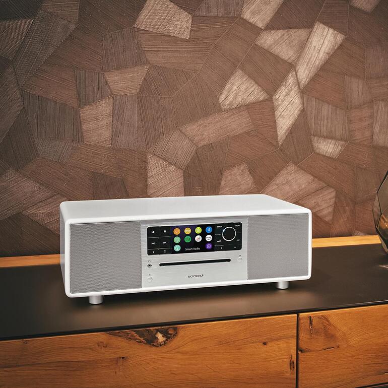 Sonoro PRESTIGE in Weiß auf einem dunklen Tisch vor Holzpanel.