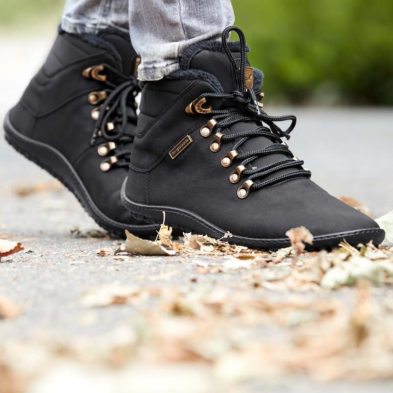 Mit diesen winterwarmen Schnürboots geniessen Sie das besonders freie, natürliche Laufgefühl auch an kalten Tagen – im Alltag, beim Einkaufsbummel, Städtetrip, Wald-Spaziergang, ... Schwarze Winter-Schnürboots mit goldenem Detail und Schnürsenkeln auf grauem Boden.