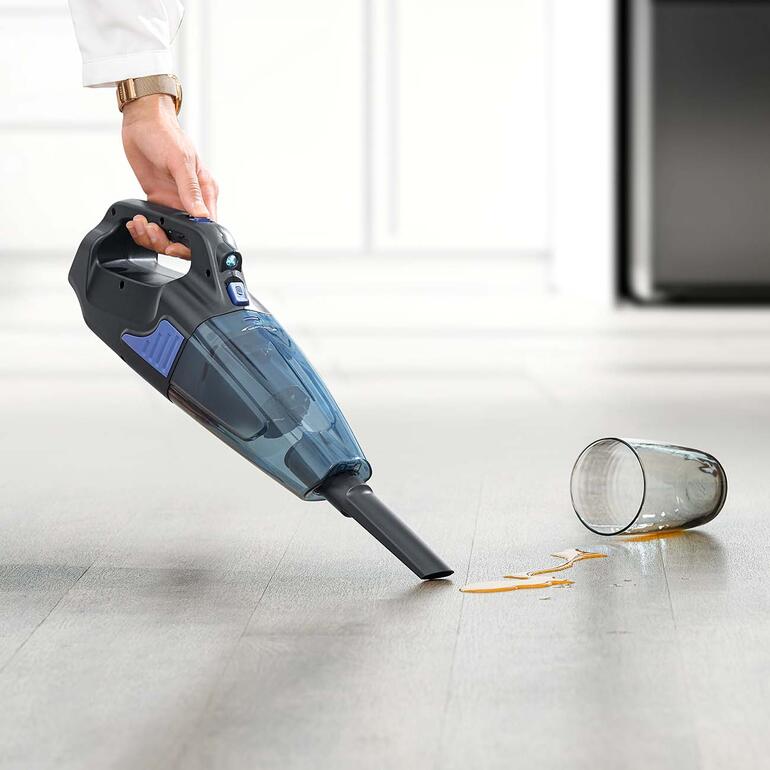 Akku-Handsauger in der Hand, saugt verschütteten Saft auf einem Holzfußboden.