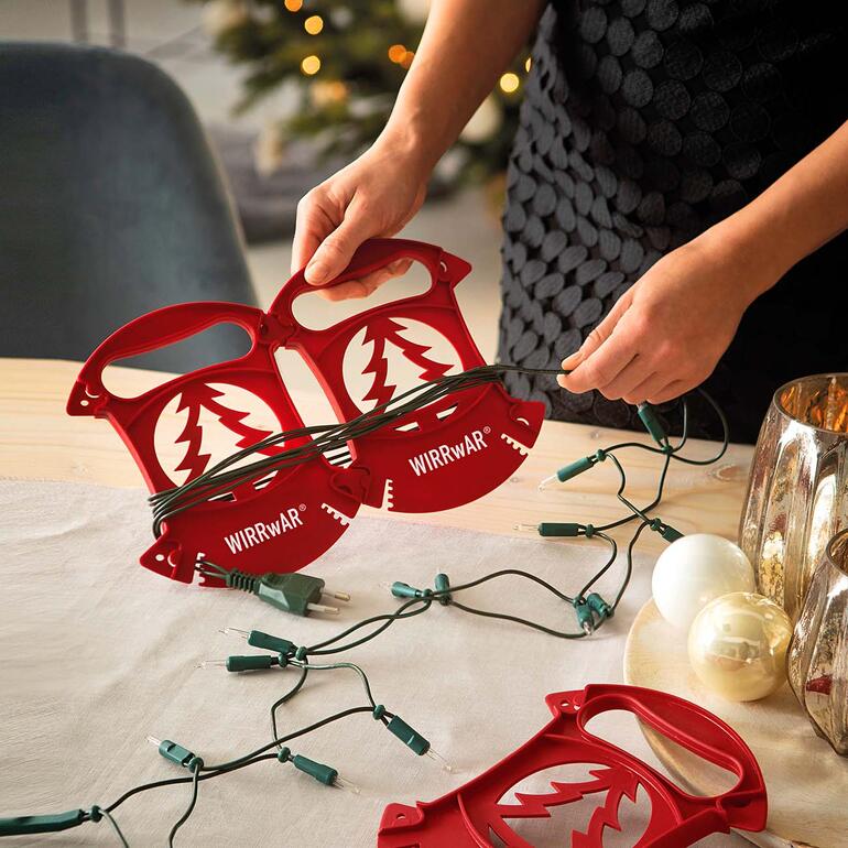 Dank patentiertem Stecksystem einzeln oder zusammengesteckt verwendbar. Person wickelt Weihnachtslichter mit WIRRwAR-Aufwickler auf einem Tisch.