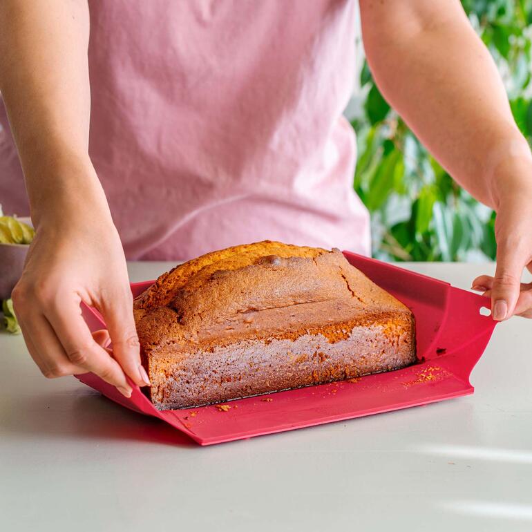 Eine Person nimmt einen frisch gebackenen Kuchen aus roter Silikonbackform.