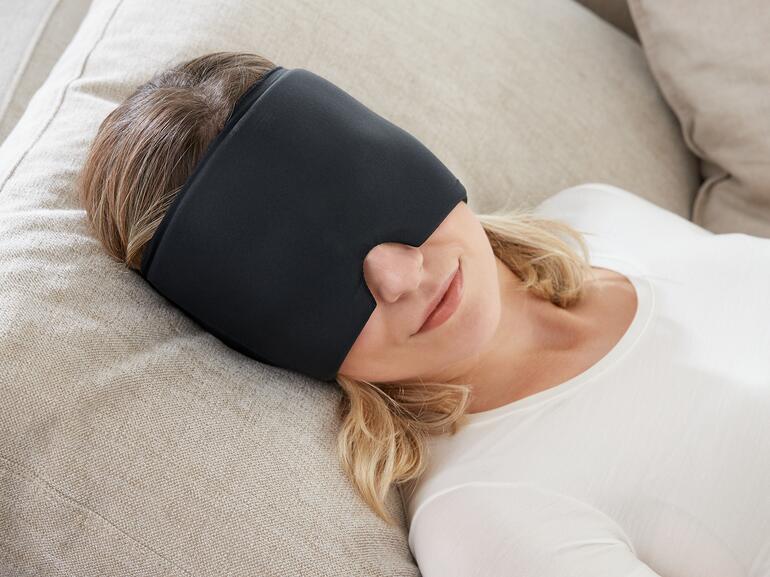 Frau mit schwarzer Augenkompresse entspannt auf einer Couch.