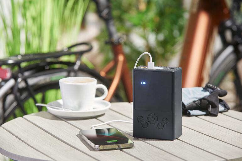 Akku-Kompressor-Luftpumpe lädt ein Smartphone auf einem Tisch.
