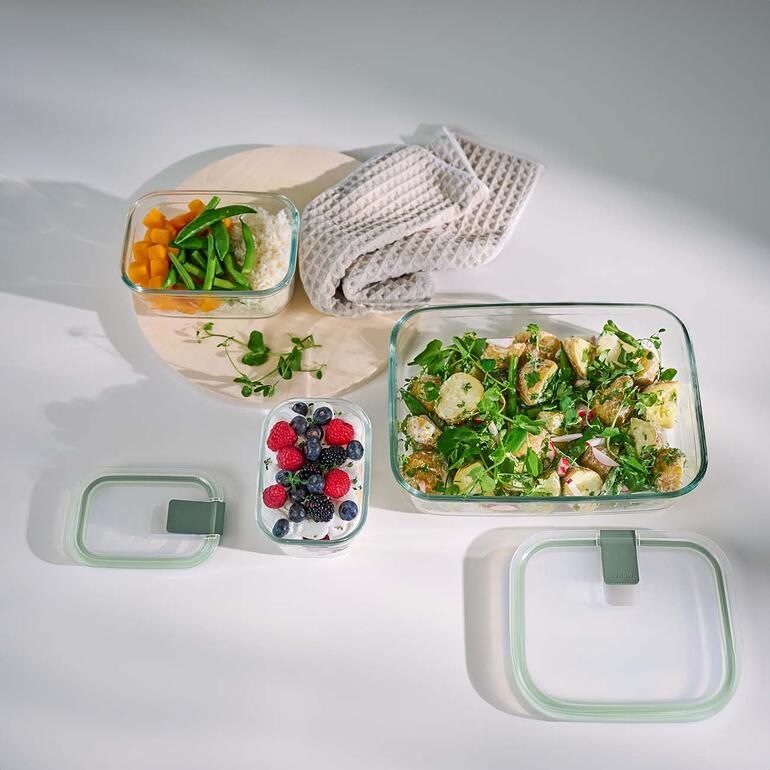 Ideal auch zum Backen, Gratinieren, Servieren, ... Verschiedene Glas-Frischhalteboxen mit Essen auf einem Tisch.